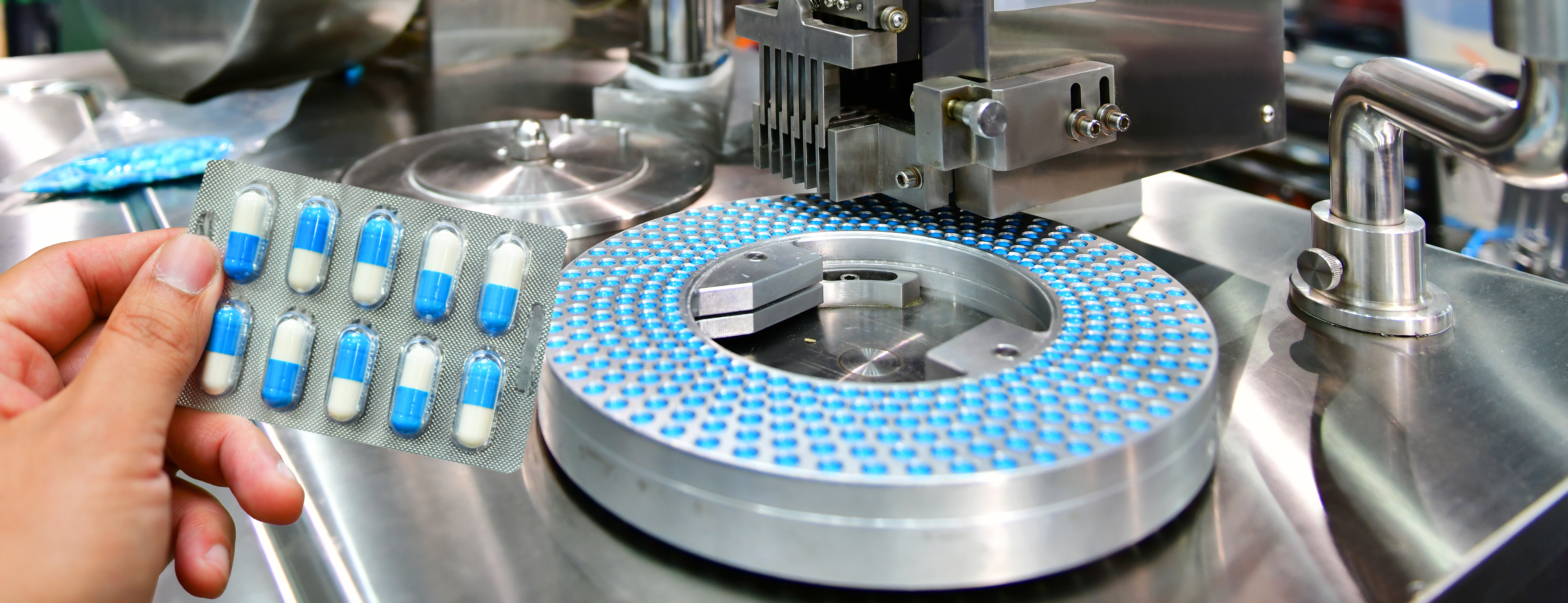 Hand holding blue capsule pack at medicine pill production line, Industrial pharmaceutical concept.banner side